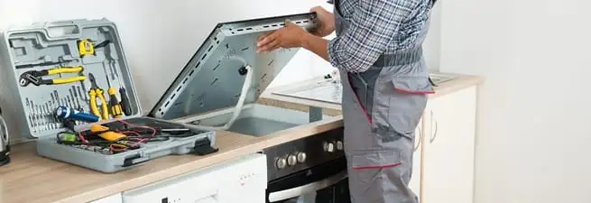Cooktop repair technician lifting a built-in stovetop for service in Lincoln, NE