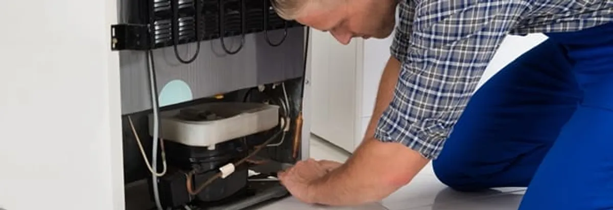 Refrigerator repair technician servicing the compressor and condenser area in Lincoln, NE