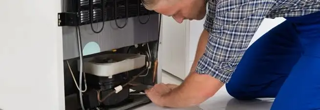 Refrigerator repair technician servicing the compressor and condenser area in Lincoln, NE