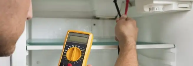 Refrigerator repair technician testing electrical components with a multimeter in Lincoln, NE