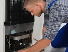 Refrigerator repair technician servicing the compressor and condenser area in Lincoln, NE